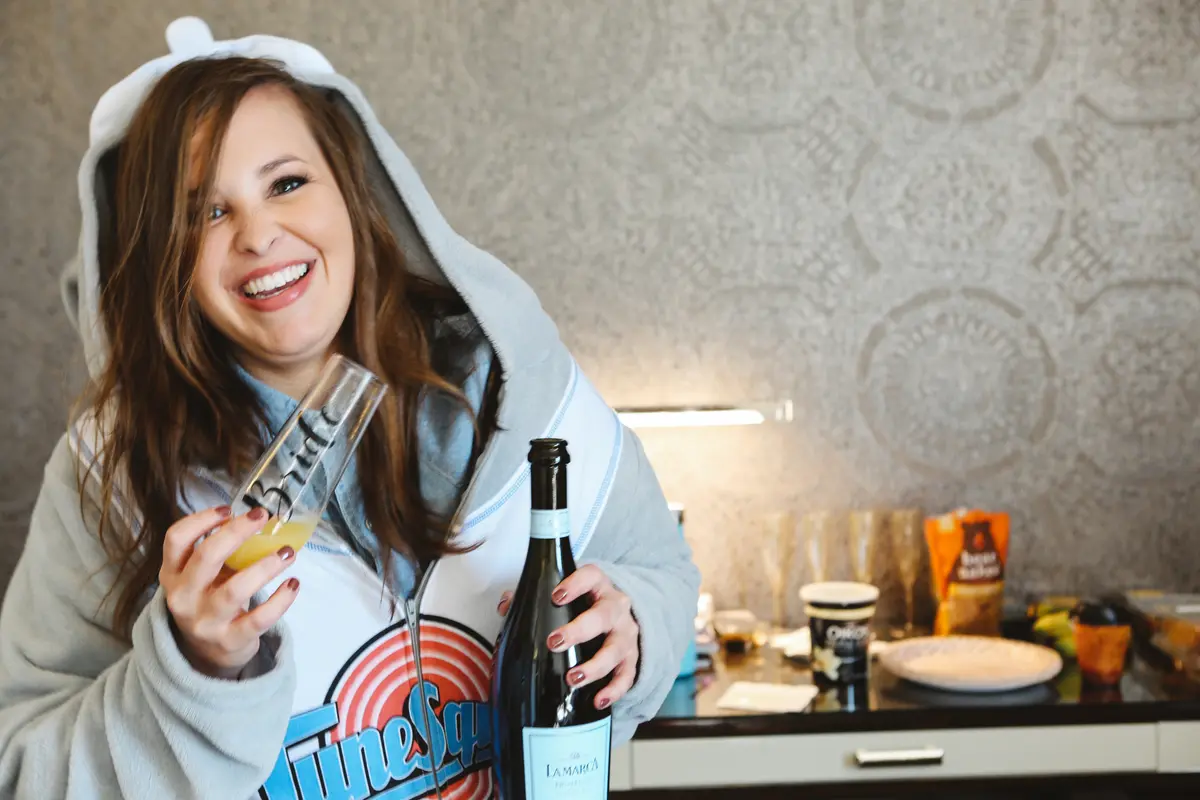 Bride laughing in a cozy hoodie, holding a glass and champagne bottle