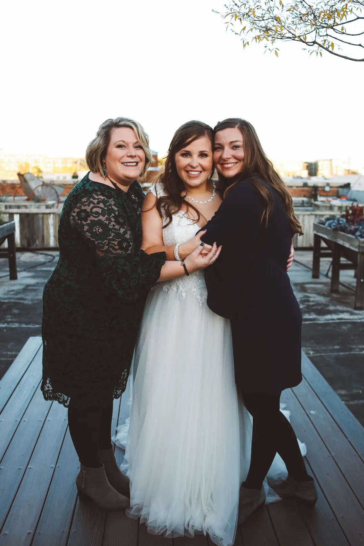 Bride hugging two of her favorite people on a rooftop on her wedding day