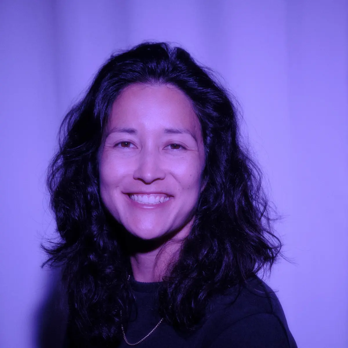 Carly Midori, San Diego family photographer, smiling in a portrait lit with soft violet light
