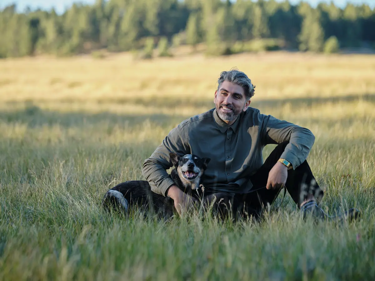Man sitting in tall grass with the couple’s dog during an engagement session