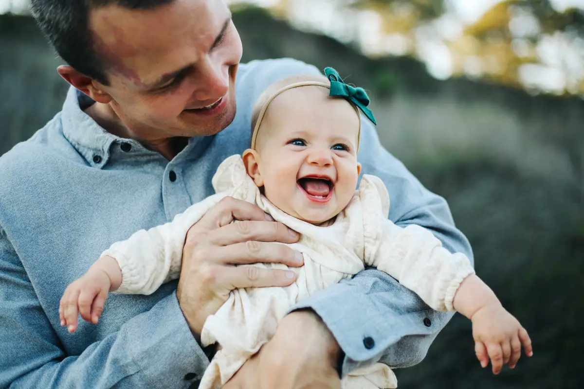 Dad holding his laughing baby girl in a green bow