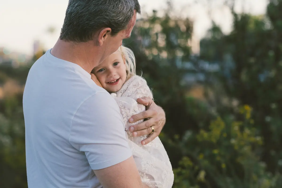Dad hugging his smiling daughter in soft golden-hour light