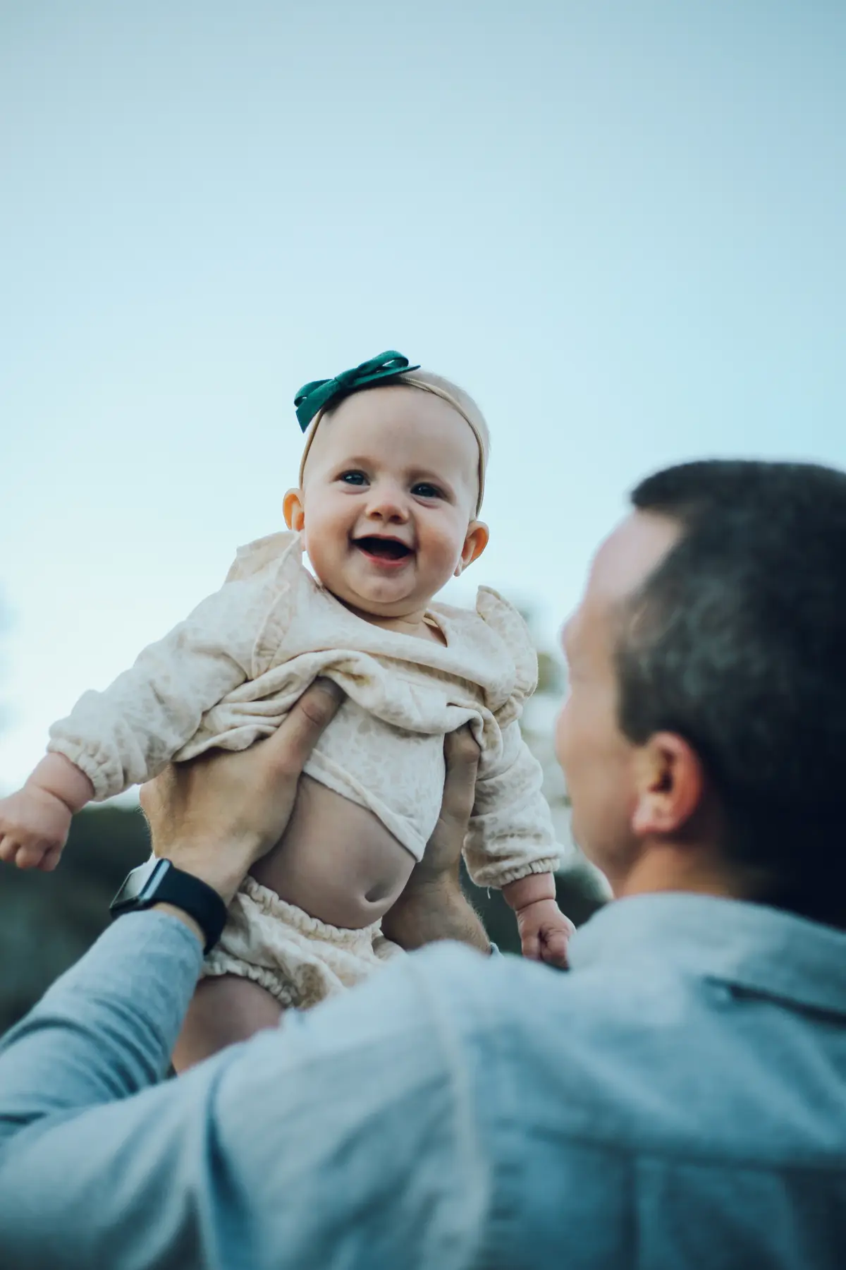 Dad lifting his smiling baby up against a clear blue sky