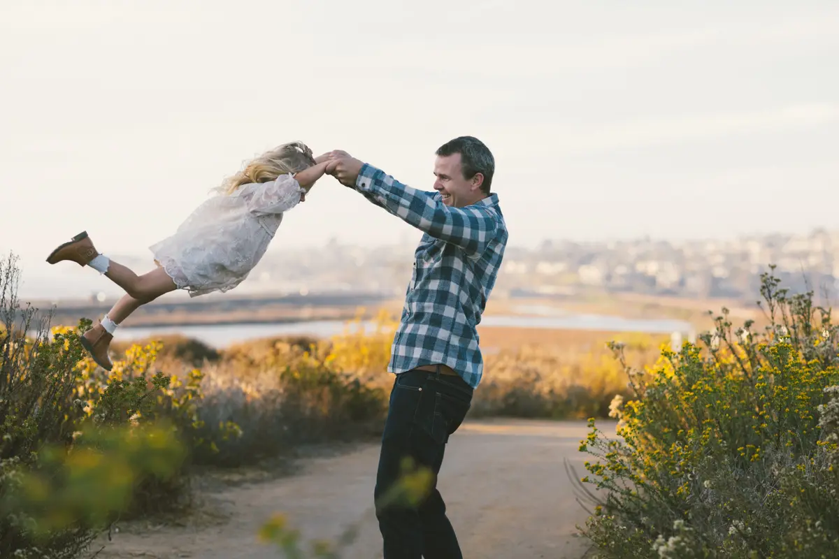Dad swinging his daughter through the air on a coastal trail above the bay