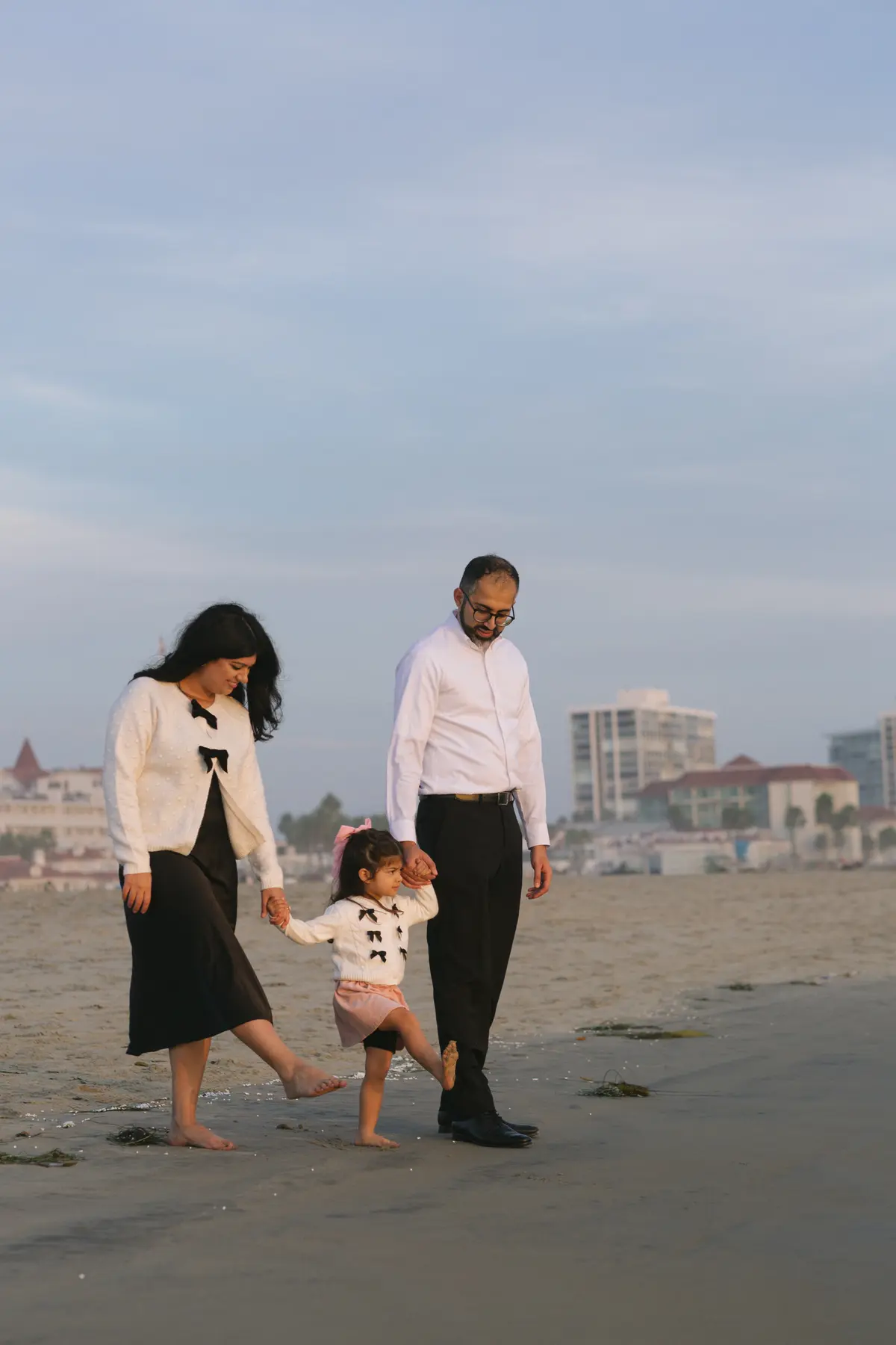 Family walking barefoot along Coronado Beach with their toddler between them