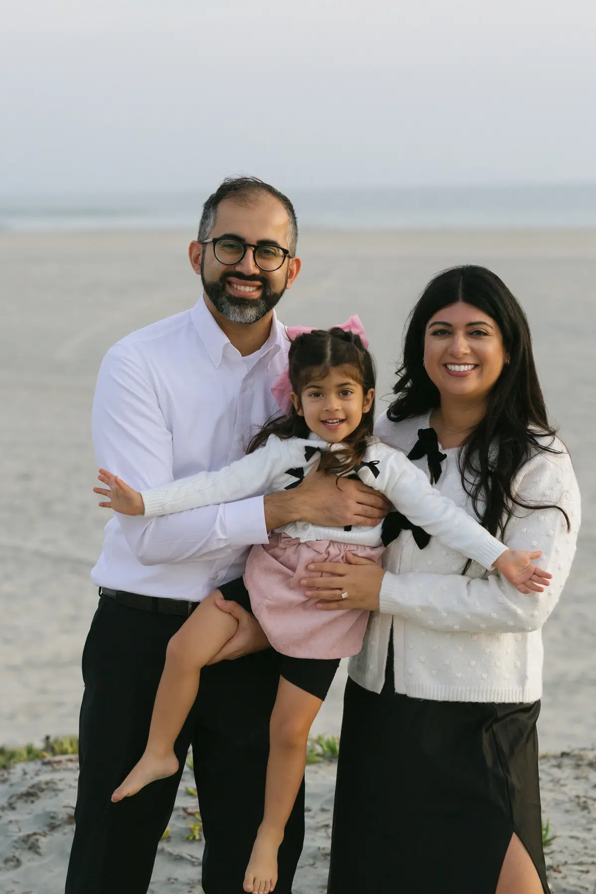 Parents holding their daughter between them on the beach for a holiday card photo