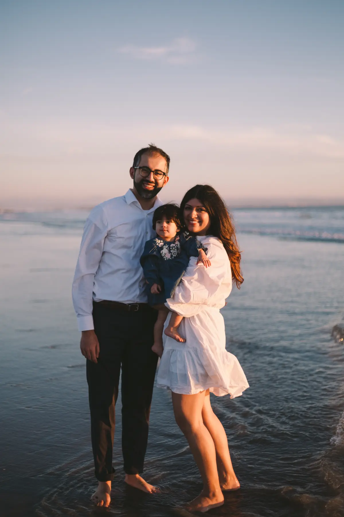 Family of three standing in the shallow surf at sunset in San Diego