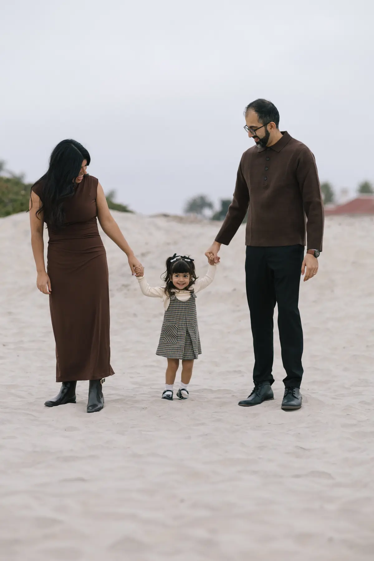 Parents holding their toddler’s hands on a walk across Coronado Beach