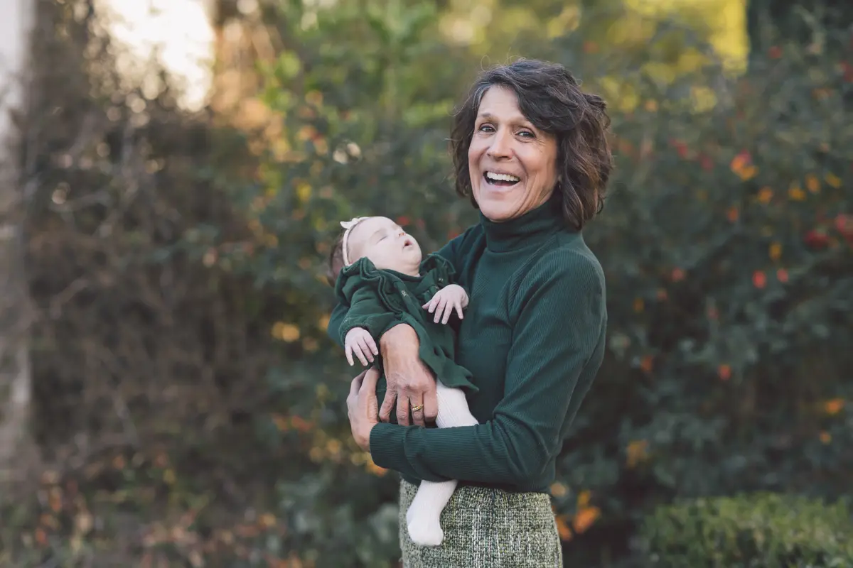 Grandmother laughing as she holds her baby grandchild in a garden