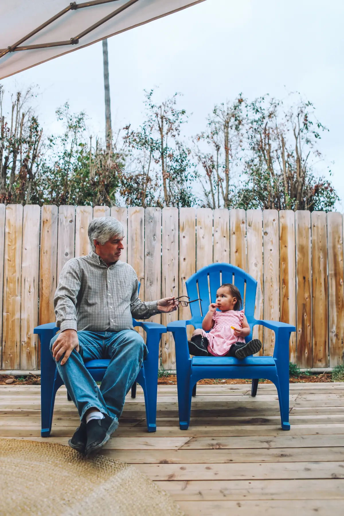 Grandpa and his toddler granddaughter sitting in matching blue Adirondack chairs