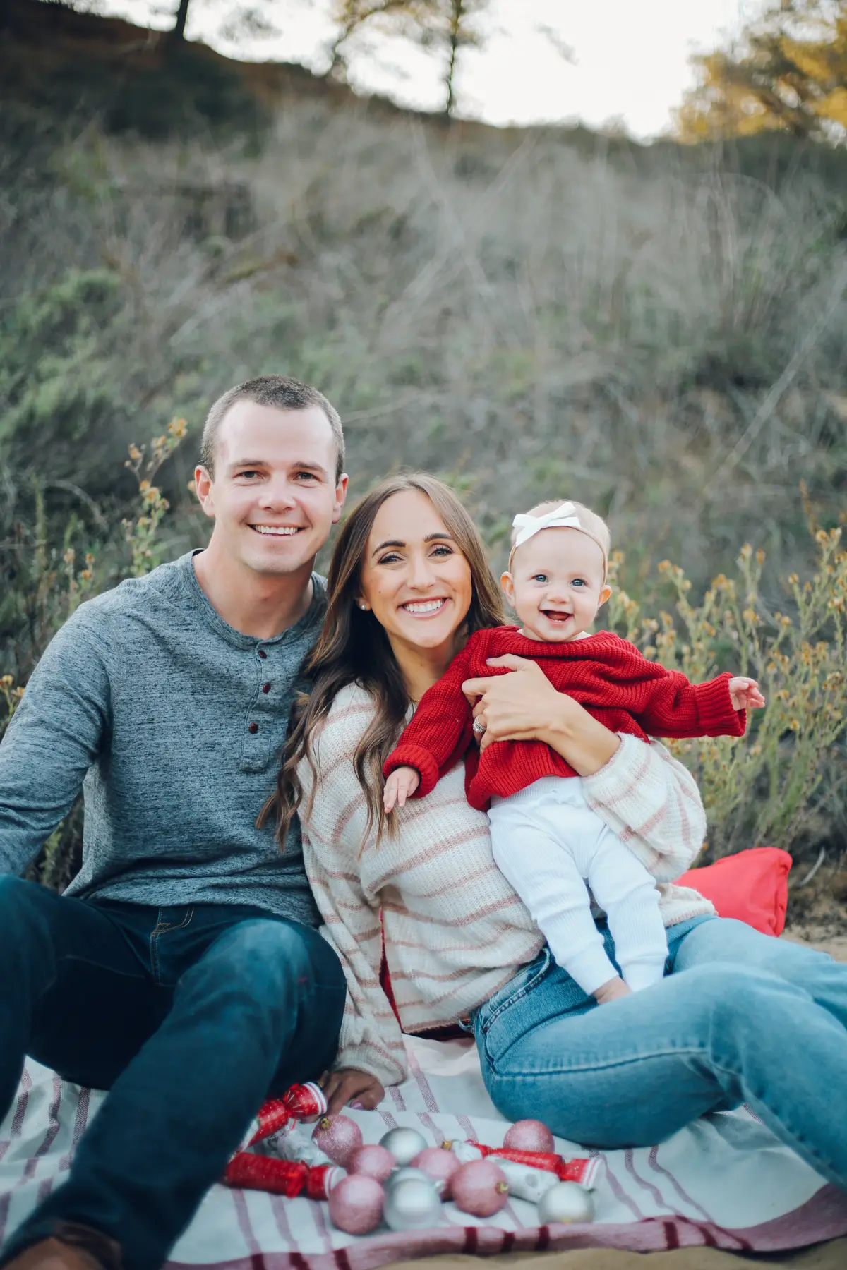 Family sitting on a blanket with holiday ornaments, baby in a red sweater