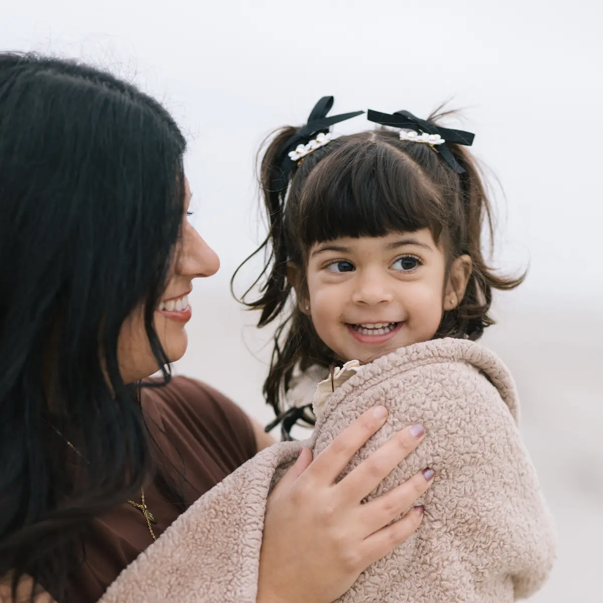 Mother and daughter sharing a smile, wrapped in a cozy blanket on Coronado Beach