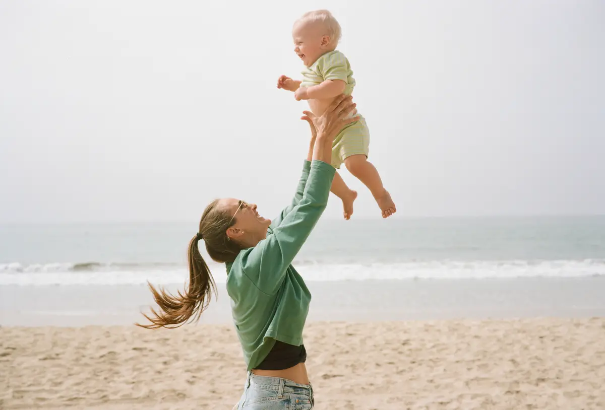 Mom tossing her laughing baby into the air on the beach