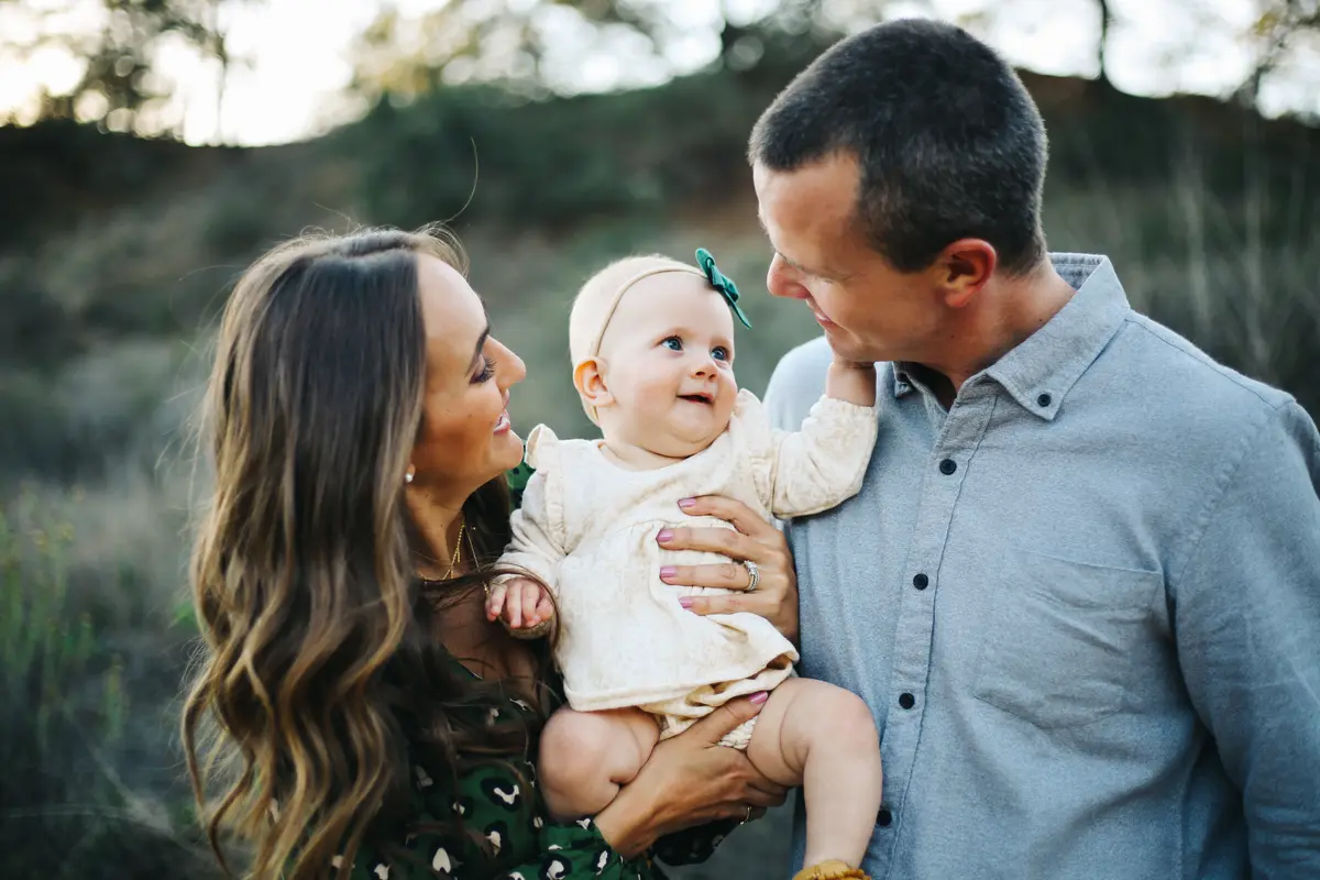 Parents smiling at their baby daughter on a grassy hillside