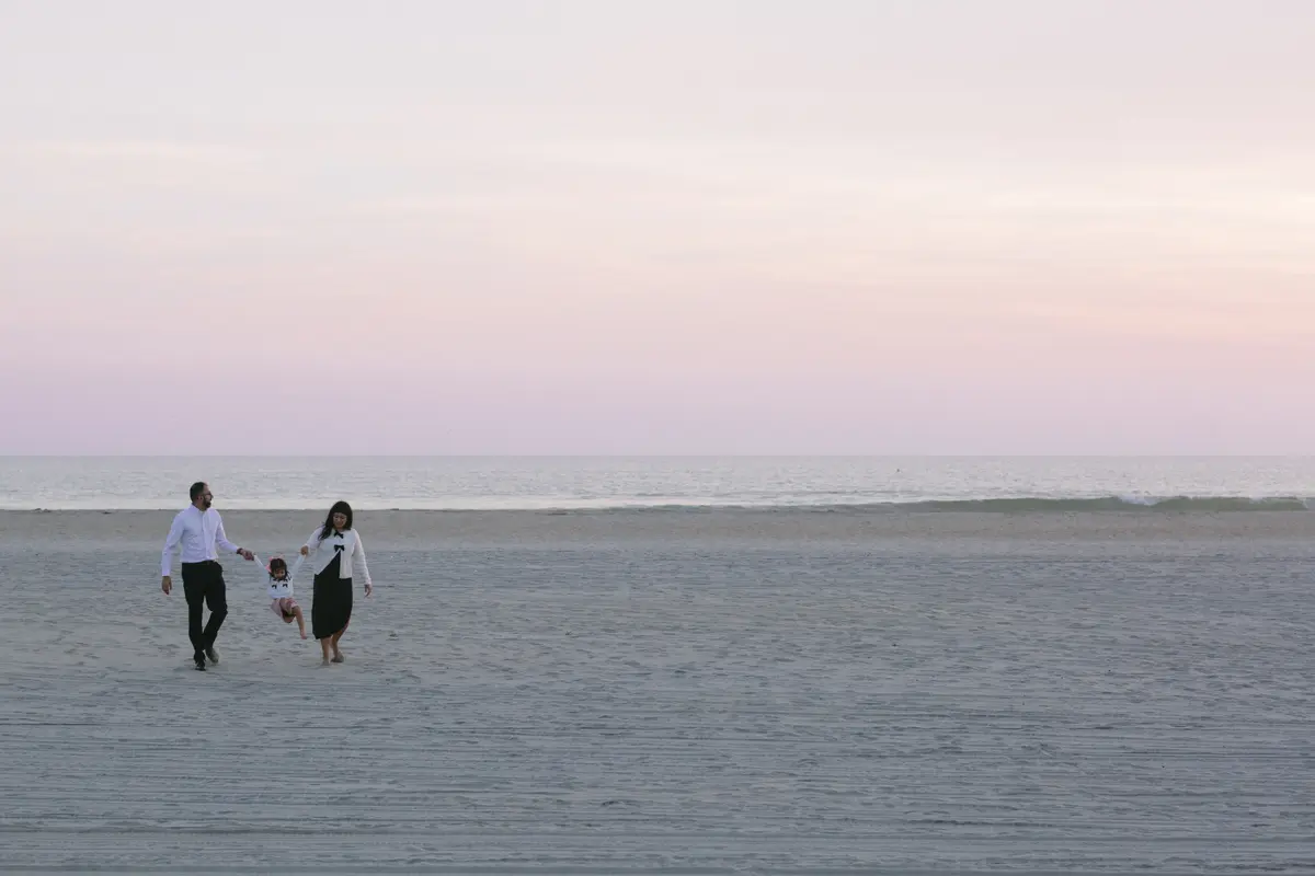 Family walking hand in hand along a wide San Diego beach under a pink sunset sky