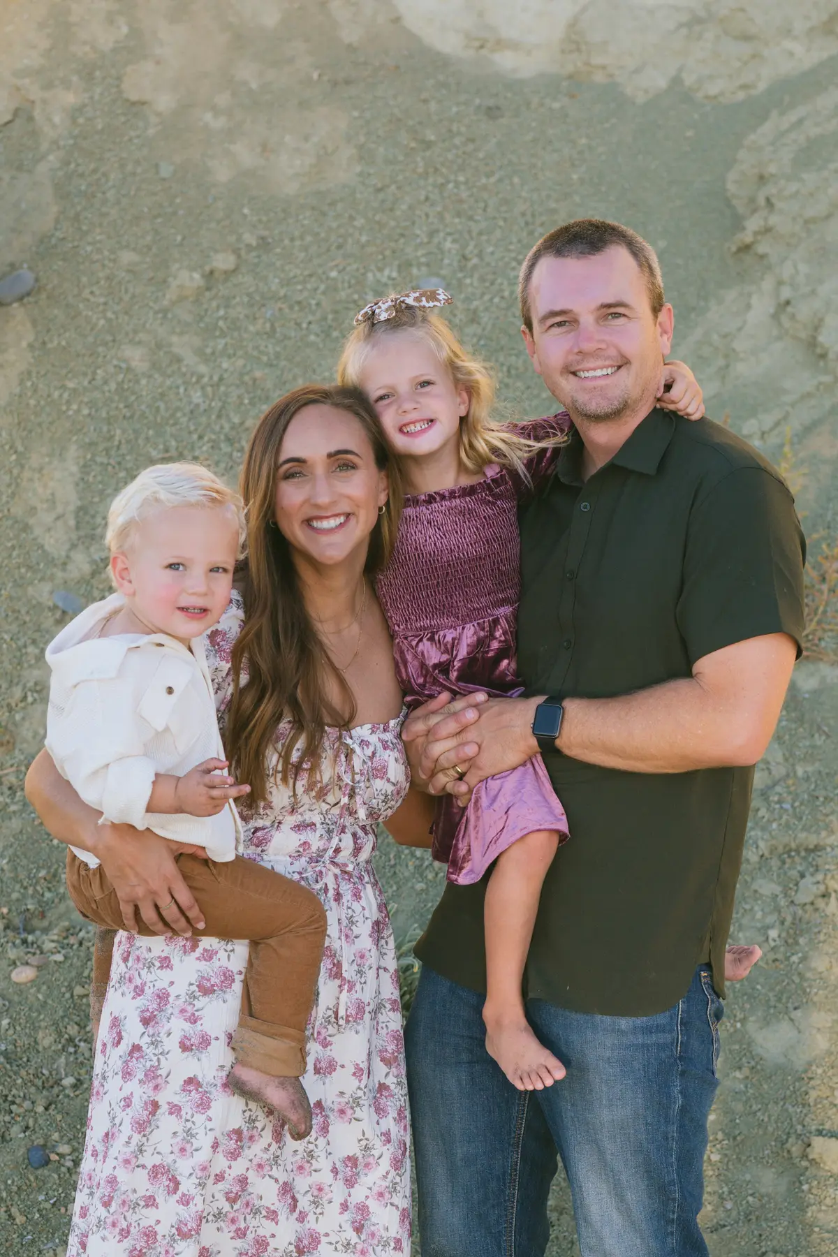 Family of four smiling together in front of sandstone bluffs for their holiday photos