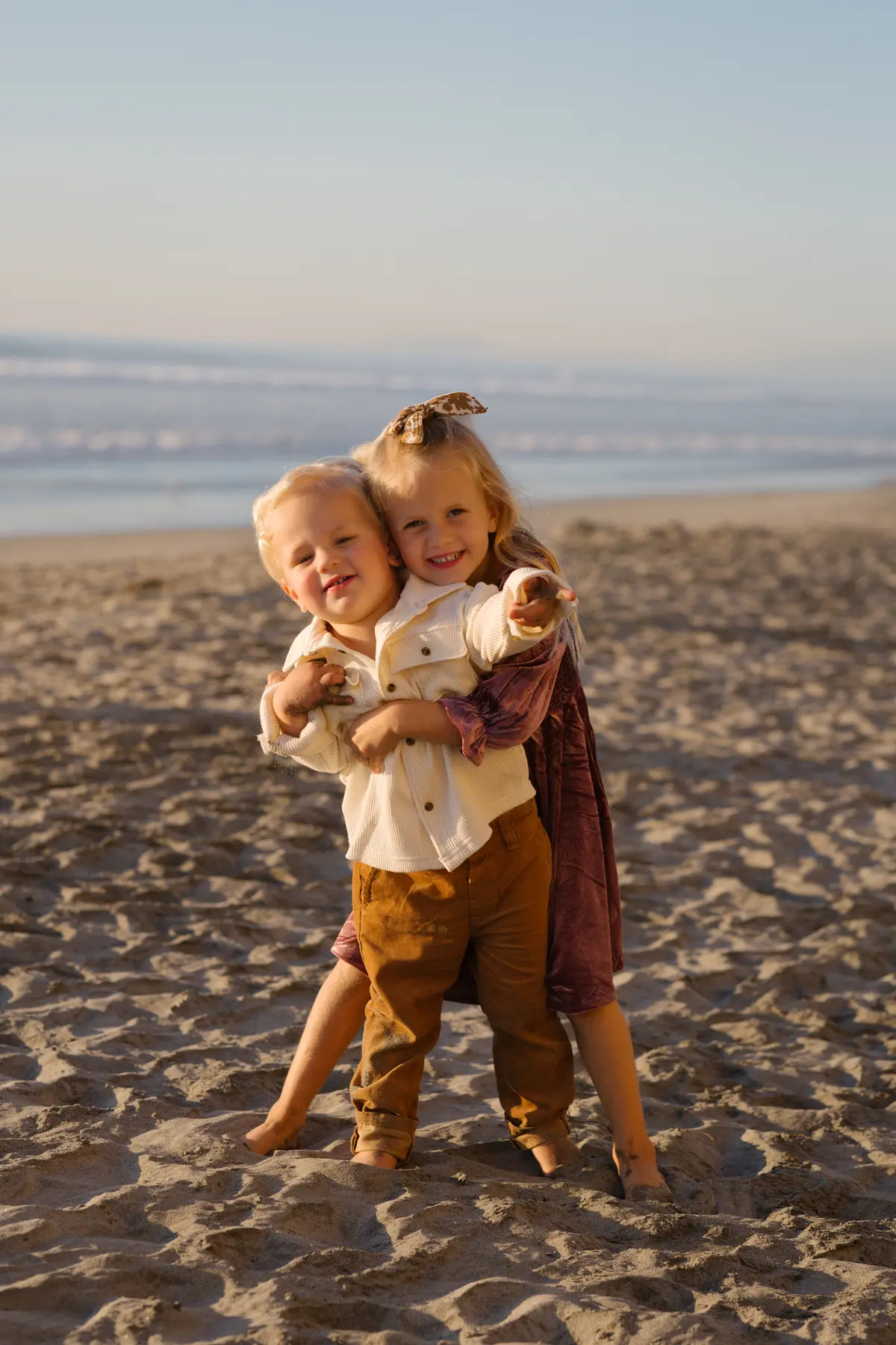 Siblings hugging on the sand at sunset during a San Diego holiday session